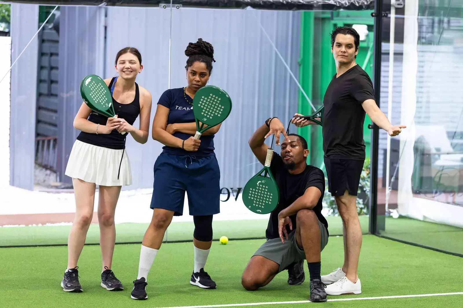 Four people posing playfully on a green padel court, holding green padel rackets